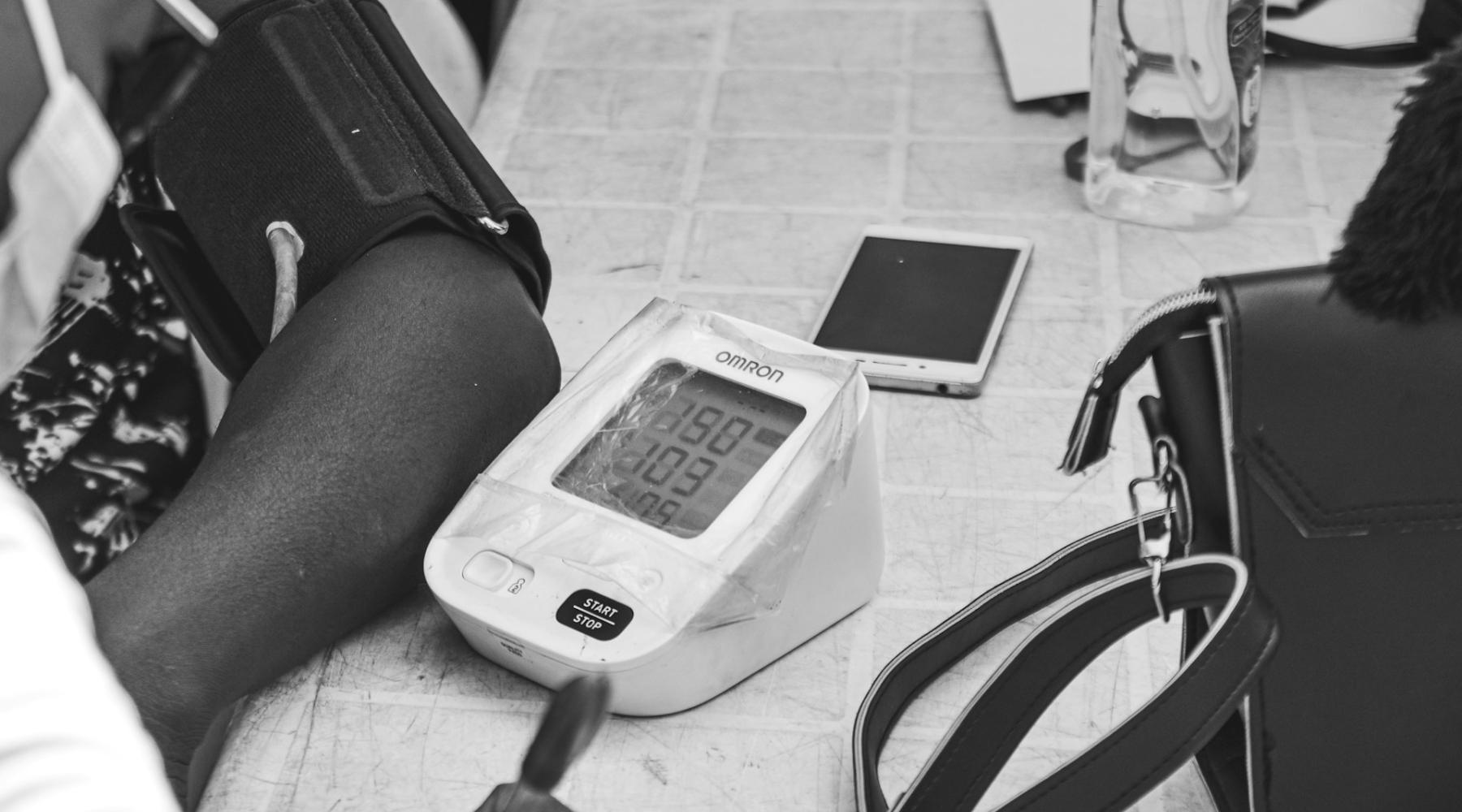 An arm rests next to a blood pressure monitor and a smartphone.