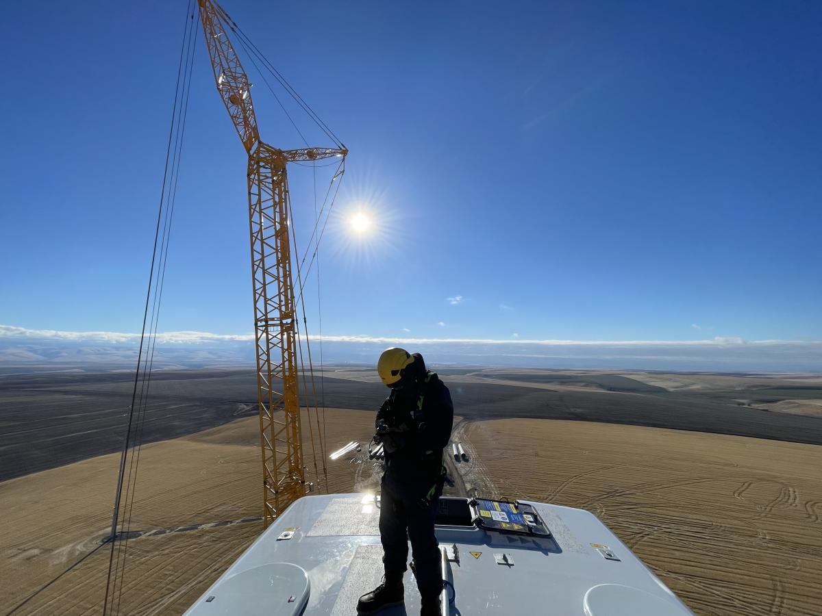 Worker standing on top of a machine at high height with a crane and the blue sky behinf him