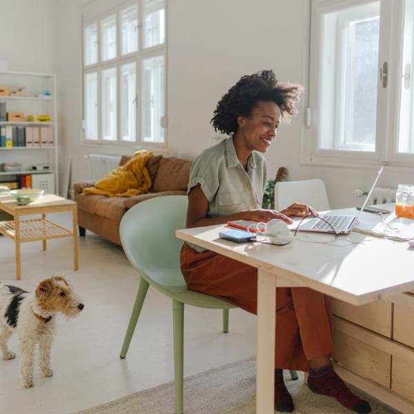 A young woman works from home as her dog looks on