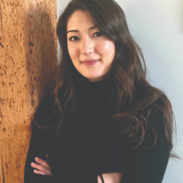 friendly and professional woman leans against wall with arms crossed looking at camera