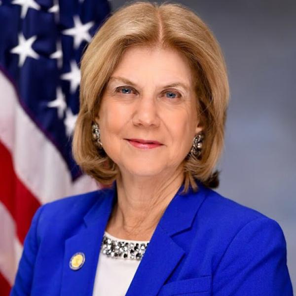 woman smiles at camera with an american flag backdrop