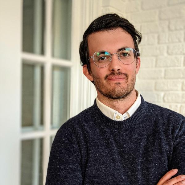 Image of Will Tucker, man with glasses wearing a blue sweater with his arms crossed