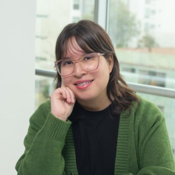 Professional headshot of a smiling woman wearing glasses and a green cardigan, seated in a bright office setting.