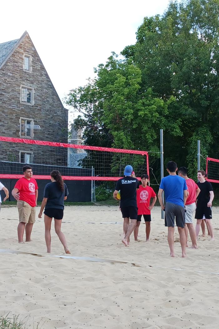 students gather in a sand volleyball court