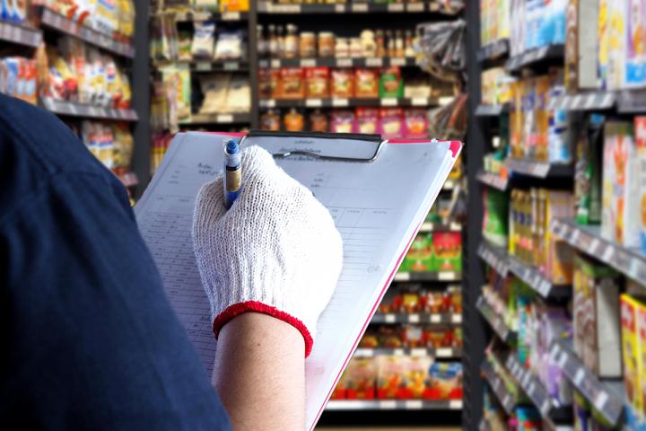female employee holding a clipboard checks products on shelves