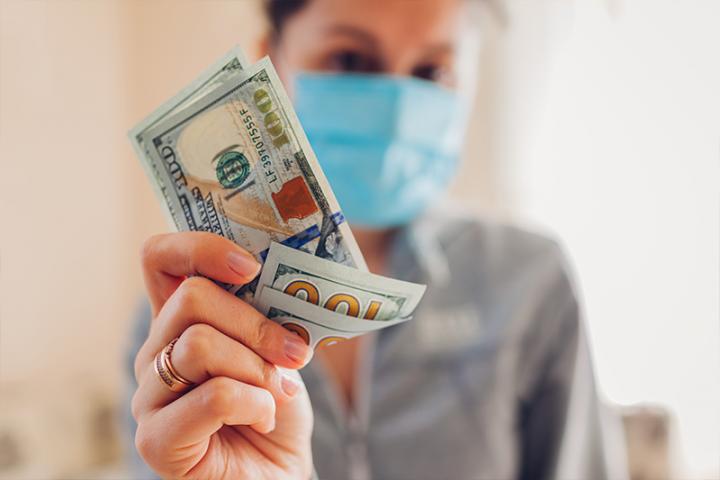 woman wearing surgical mask holding several hundred dollar bills