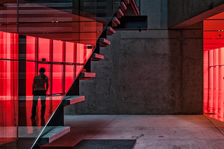 Silhouette of a person through red glass on a hotel stair landing.