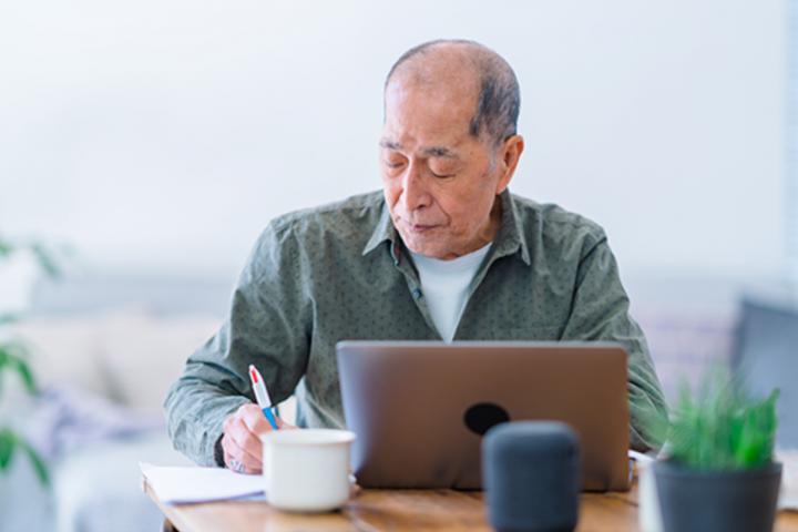 Older man working at desk on a laptop computer.