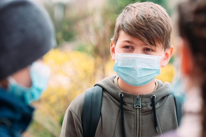 A young boy is wearing a medical mask talking with friends at school.