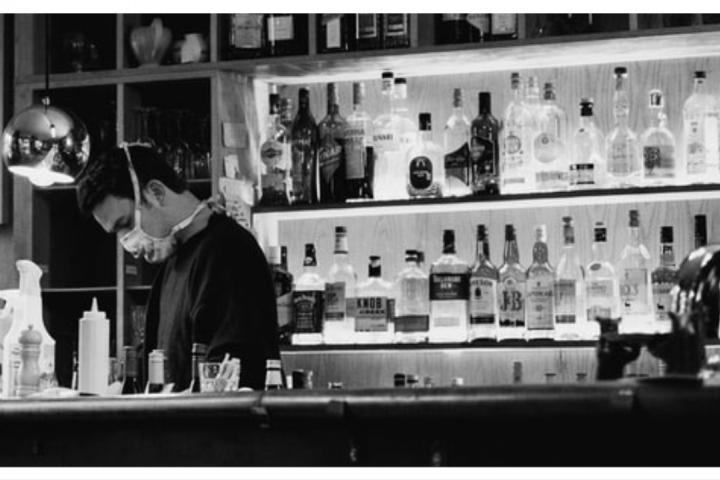 person wearing a mask working behind a bar at a restaurant