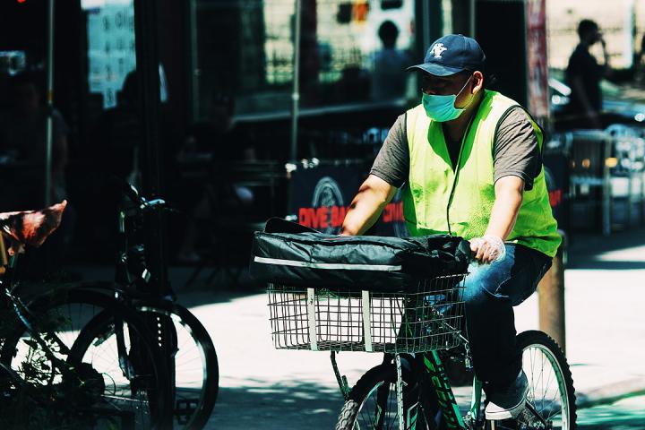 man wearing a mask and high-vis vest riding a delivery bike