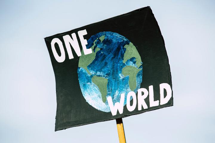 sign on a post saying: "one world" over a graphic of the globe to illustrate unity and the planet
