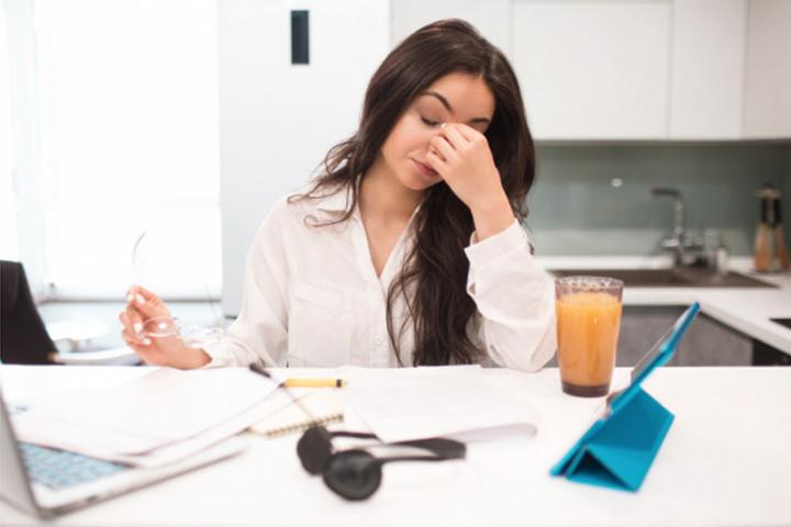 Frustrated young woman working at home. She is holding her glasses and is leaning her head on her hand.
