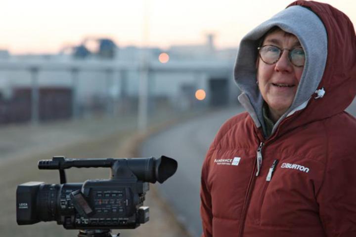 Filmmaker Julia Reichert outside on a cold morning with a video camera.