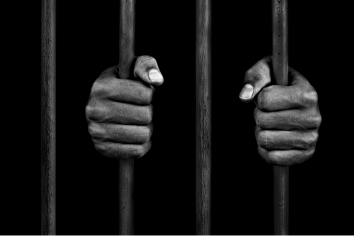 Two Black hands holding prison bars