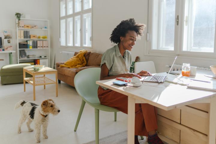 A young woman works from home as her dog looks on
