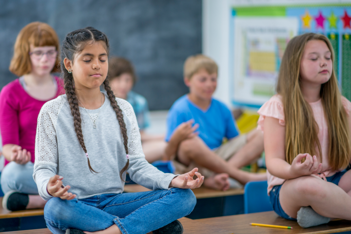A group of middle school students meditating on their desk. 