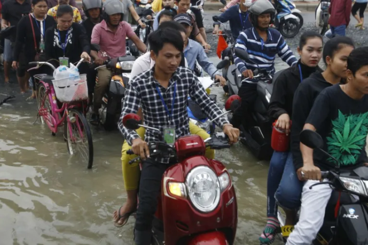 Person riding scooter through crowded, flooded street. 