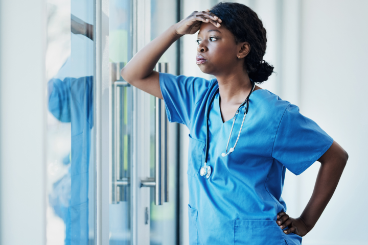 A tired Black nurse looks out a window