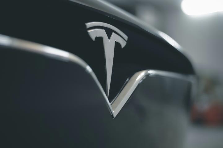 Close up of Tesla logo on front grill of gray Tesla car