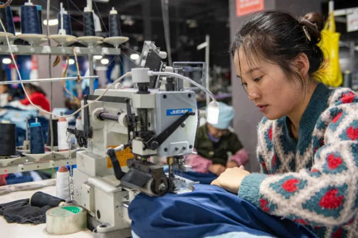 Person at sewing machine in a large factory.