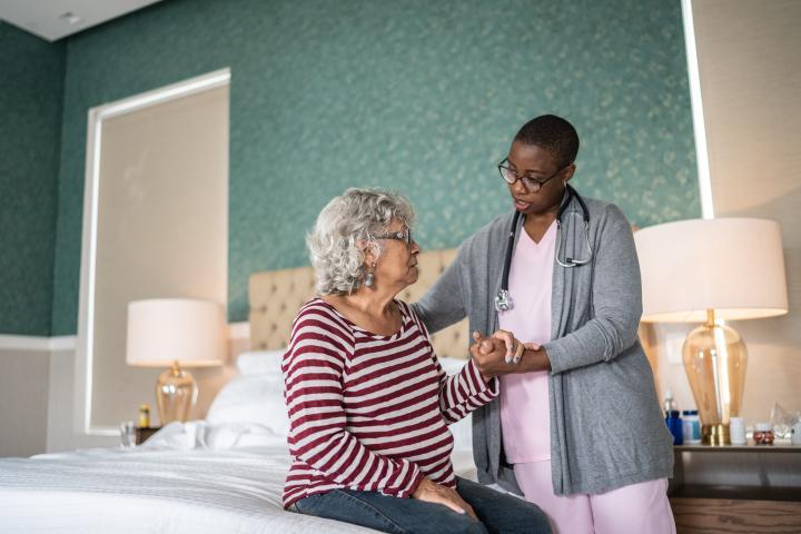 Home care worker standing next to elderly patient assisting them sitting up