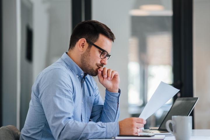 An office worker reviews a sheet of paper while seated at a table.
