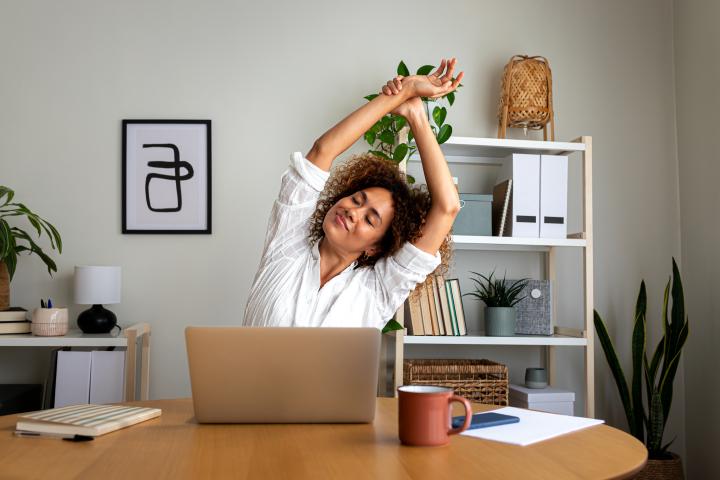 Woman sitting at desk with laptop in front of her, stretching with arms above her head.