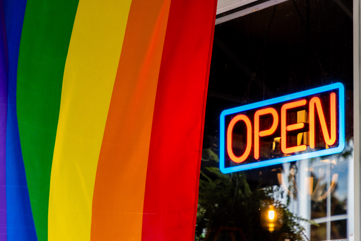 A pride flag hangs next to and open for business sign. 