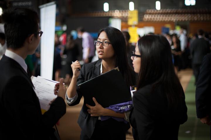 Students in professional attire speak with a recruiter while holding résumés and portfolios at a crowded career fair in Barton Hall.