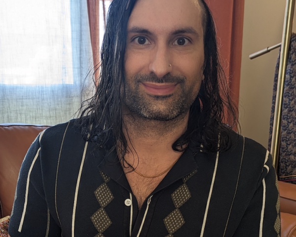 Image of a man with dark hair smiling at the camera, wearing a green button up shirt.