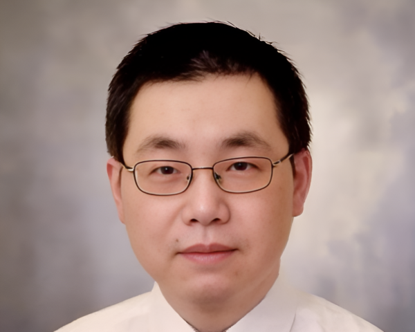 Professor Sheng Lu sits, wearing a white shirt and a dark tie. He wears glasses and has short dark hair.