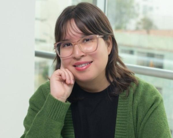 Professional headshot of a smiling woman wearing glasses and a green cardigan, seated in a bright office setting.