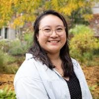 Fall foliage as background, dark haired, Asian woman, glasses, black shirt under jean button up