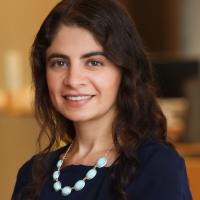 Marina Severinovsky wears a dark dress with a white, peal necklack. She has brown curly hair down to her shoulders.