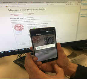 Someone holding their iPhone to a computer screen to read the verification barcode to enroll the device as a two-step authentication device.