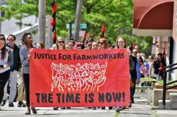 Protest marchers carry a banner reading, Justice for Farmworkers, the time is now.