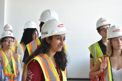 Ashni Verma stands with a group of High Road Fellows wearing hard hats and listening to a speaker.