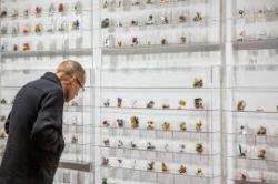 Man closely inspecting small unidentifiable objects arranged carefully in regular rows and columns on a white museum wall.
