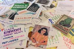 Scattered pile of bumper stickers, postcards, notes reading, Defend our Democracy, Anne Frank, Make Empathy Great Again - Ithaca welcomes refugees, etc.